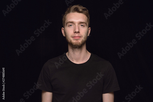 Close up portrait of young caucasian man isolated on black studio background. Photoshot of real emotions of male model. Standing and looks serious. Facial expression, human nature and emotions concept © master1305