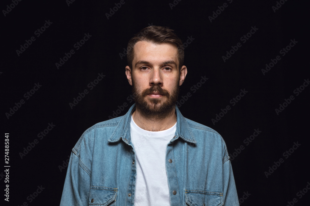 Obraz premium Close up portrait of young caucasian man isolated on black studio background. Photoshot of real emotions of male model. Standing and looks serious. Facial expression, human nature and emotions concept