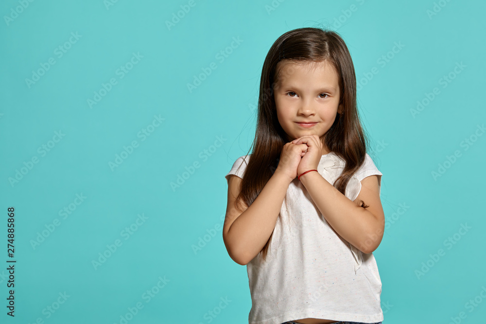 Close-up shot of a cute brunette little girl in a white blouse posing against a blue background. Close-up shot of a cute brunette little girl in a white blouse posing against a blue background.