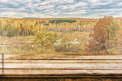 Empty wooden table with picturesque autumn landscape of view from the hill to the lowland with forest and swamps. Mock up for display or montage products