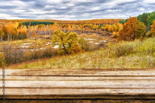 Empty wooden table with blurred picturesque autumn landscape of view from the hill to the lowland with forest and swamps. Mock up for display or montage products