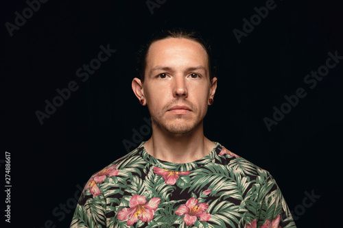 Close up portrait of young caucasian man isolated on black studio background. Photoshot of real emotions of male model. Standing and looks serious. Facial expression, human nature and emotions concept