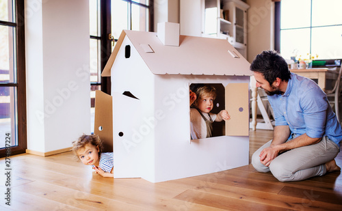 Two toddler children with father playing with paper house indoors at home. photo