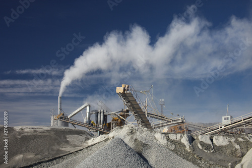 White smoke from a pipe rock stone crushing machine against a blue sky. Mining industry. Quarry mining equipment.