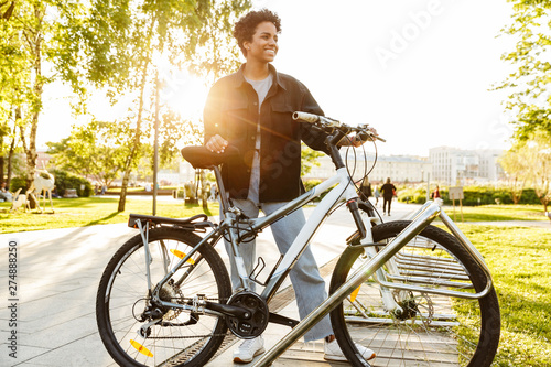 Photo of beautiful african american woman standing with bicycle while walking in city park