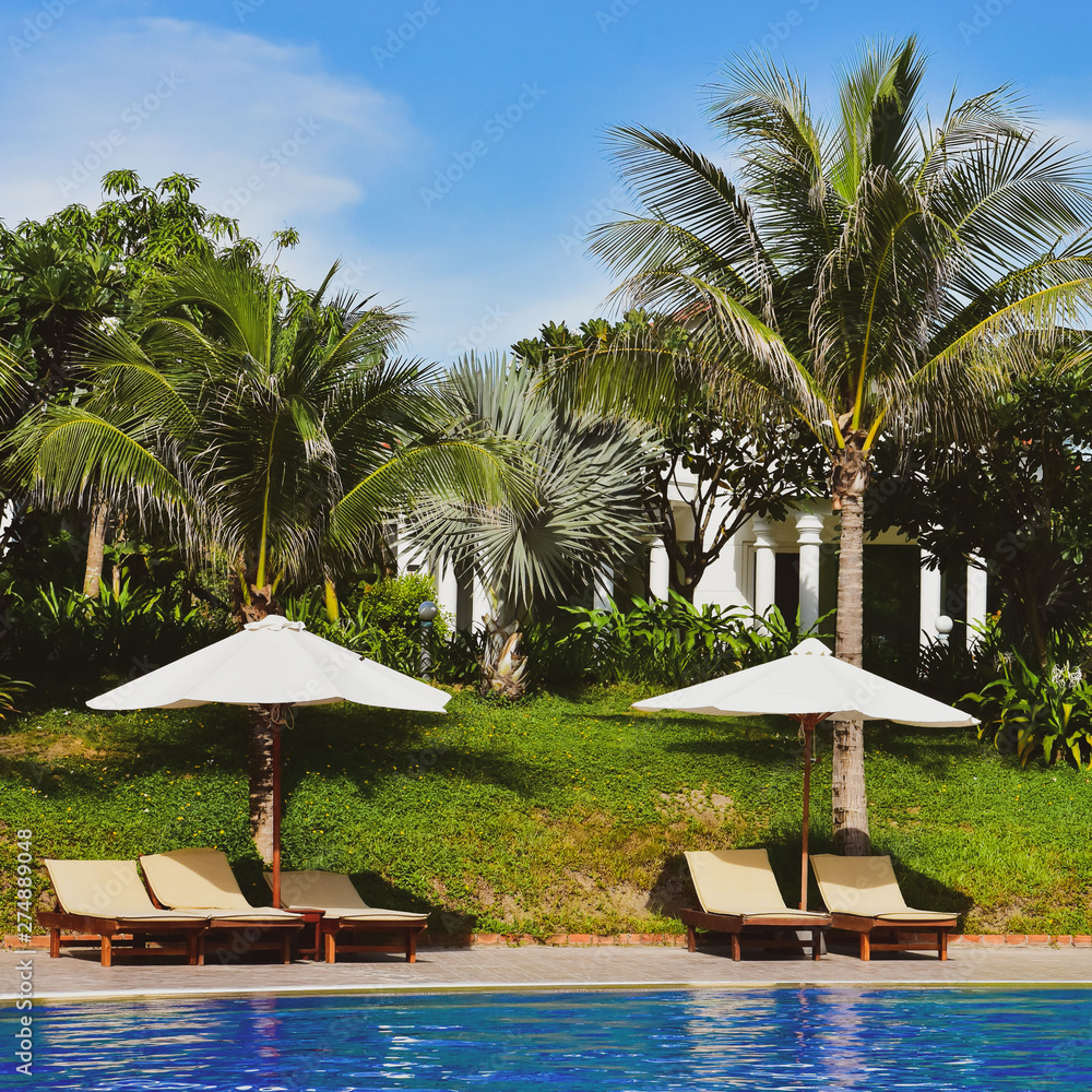 empty deck chairs with sun umbrellas next to the pool. The territory of a modern hotel in Asia. bungalow roofs behind palm trees. vintage toning