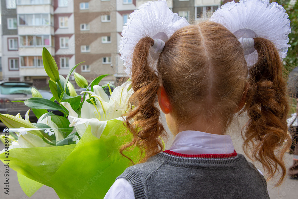 A girl with large white bows on her head, a beautiful hairstyle. She has a bouquet with lilies. She was going to go to school on September 1st. View from the back close up