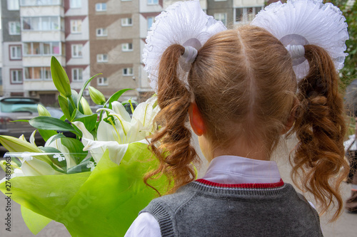 Obraz na płótnie A girl with large white bows on her head, a beautiful hairstyle. She has a bouquet with lilies. She was going to go to school on September 1st. View from the back close up w salonie