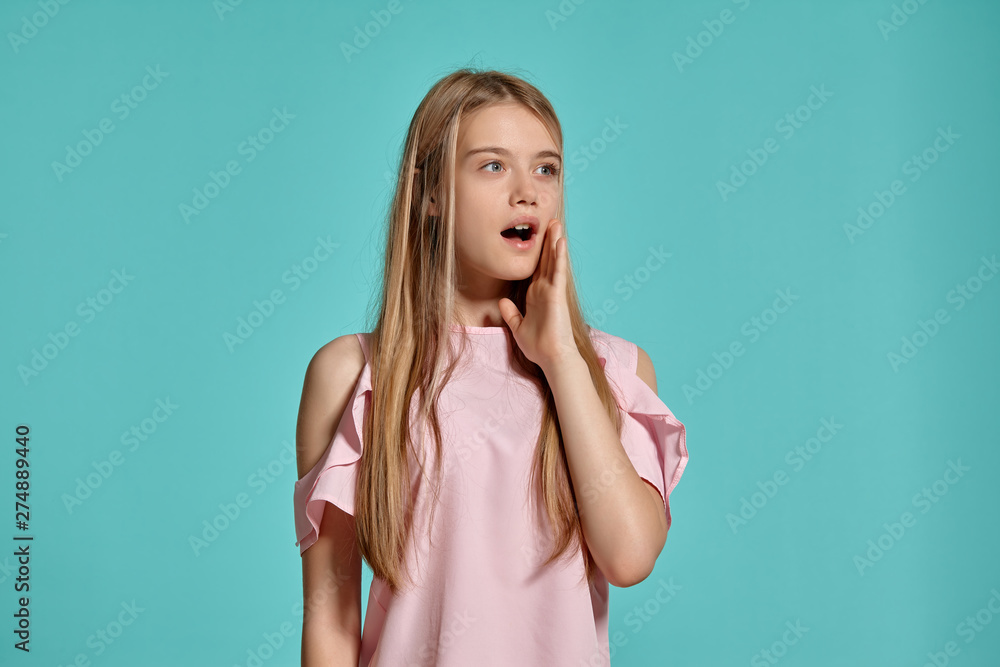 Studio portrait of a beautiful girl blonde teenager in a pink t-shirt posing over a blue background. Studio portrait of a beautiful girl blonde teenager in a pink t-shirt posing over a blue background.