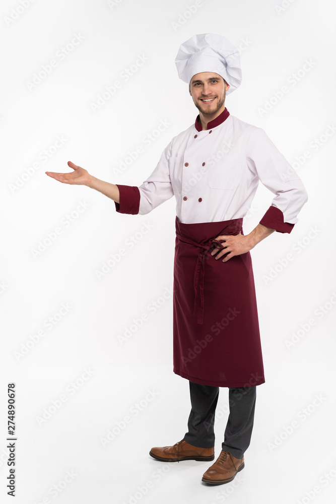 Full length of smiling young cook in uniform standing isolated over white background. Looking camera pointing. Full length of smiling young cook in uniform standing isolated over white background. Looking camera pointing.