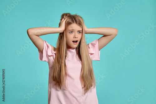 Studio portrait of a beautiful girl blonde teenager in a pink t-shirt posing over a blue background. © nazarovsergey