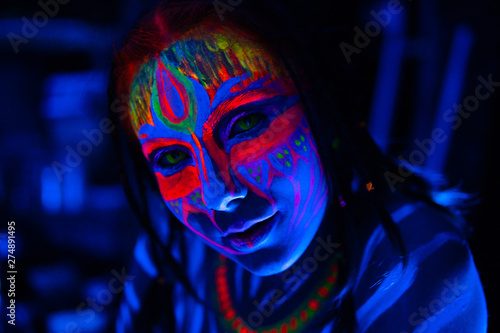 Leinwand Poster Close-up Portrait of Young naked bodyarted woman in blue glowing ultraviolet paint and Yellow eye lenses