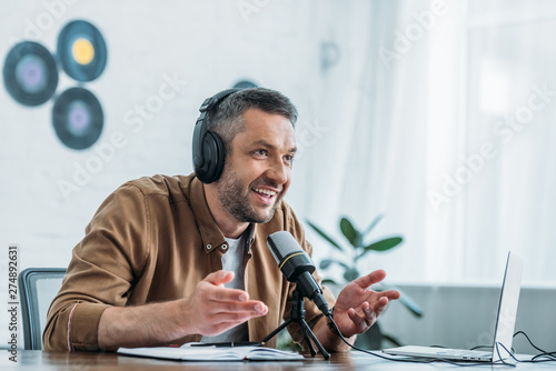 Εκτύπωση καμβά smiling radio host in headphones gesturing while speaking in microphone in broad