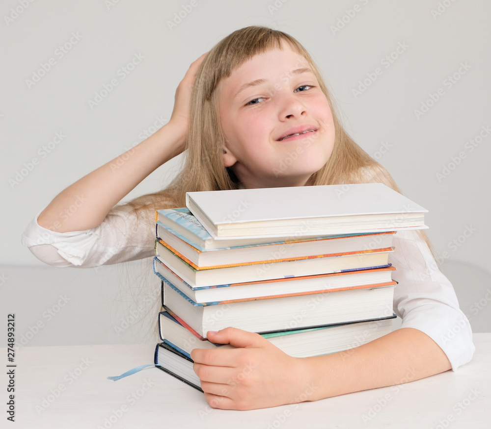 Happy little girl strokes her head and hugs a stack of books Happy little girl strokes her head and hugs a stack of books