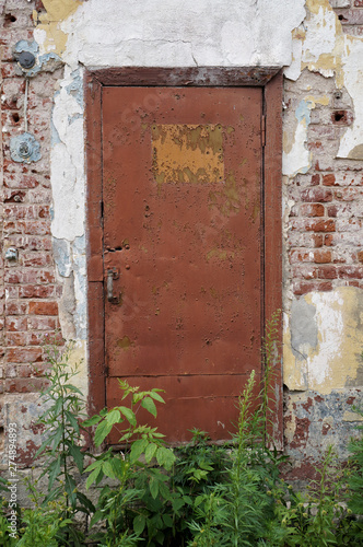 Closed old painted metal door. Symmetric front view from outside, old brick wall, brown shabby paint  © Natalia Baran