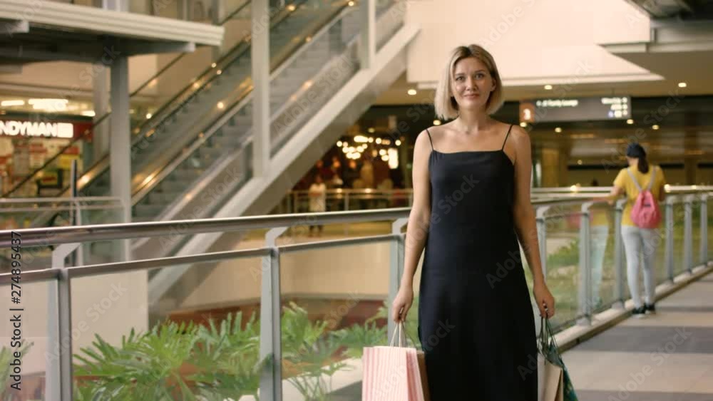 Happy blonde woman with black dress walking with several bag in mall Happy blonde woman with black dress walking with several bag in mall