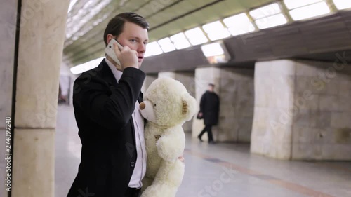 Man is talking on the phone and is waiting for his beloved, in his hand is a gift toy bear. photo