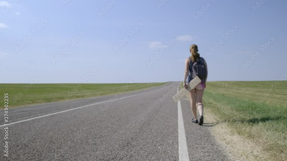 Girl traveler hitchhiking. woman walks on road with backpack and cardboard sign that says anywhere in her hands in anticipation of passing car. Girl traveler hitchhiking. woman walks on road with backpack and cardboard sign that says anywhere in her hands in anticipation of passing car.