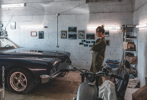 Attractive Caucasian woman looking at her vintage old car in a garage