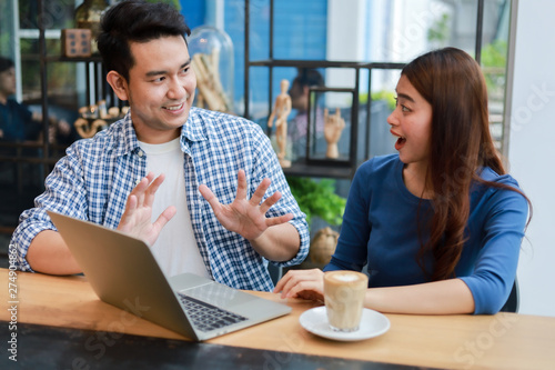 Asian couple in blue shirt drinking coffee talking and working with computer laptop smile and happy mood in coffee shop cafe