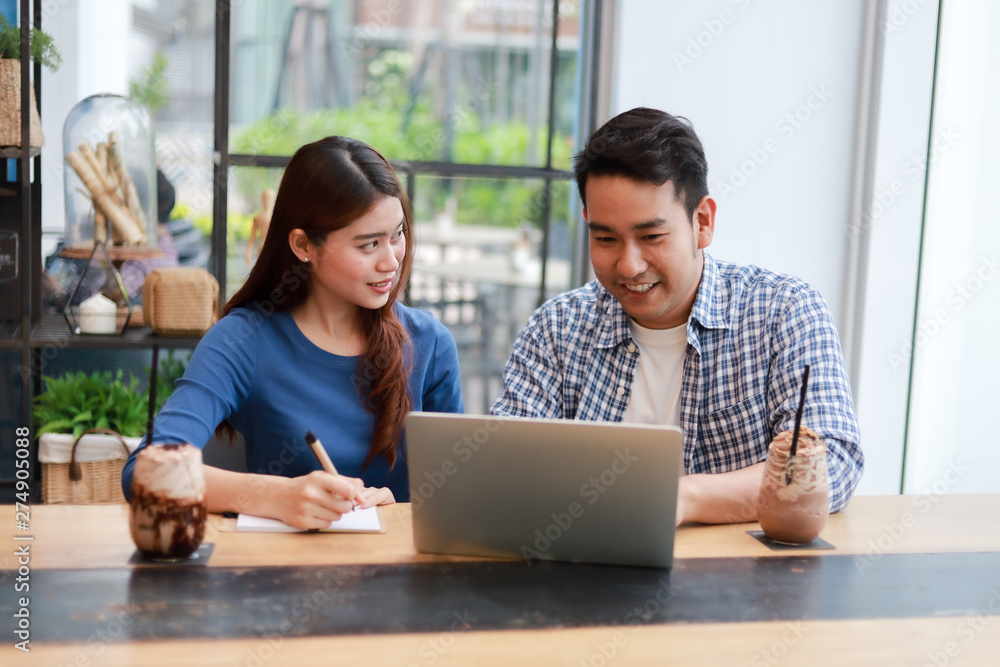 Asian couple in blue shirt drinking coffee talking and working with computer laptop smile and happy mood in coffee shop cafe Asian couple in blue shirt drinking coffee talking and working with computer laptop smile and happy mood in coffee shop cafe