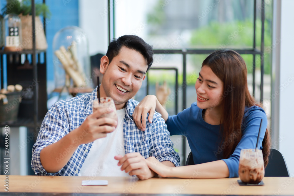 Asian couple in blue shirt drinking coffee talking and working with computer laptop smile and happy mood in coffee shop cafe Asian couple in blue shirt drinking coffee talking and working with computer laptop smile and happy mood in coffee shop cafe