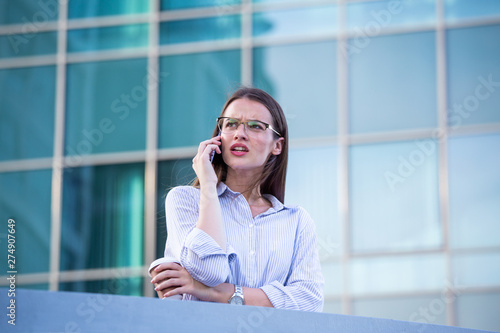 Business woman recieving bad news on smartphone and drinking coffee from disposable paper cup in the street with office buildings in the background © Graphicroyalty