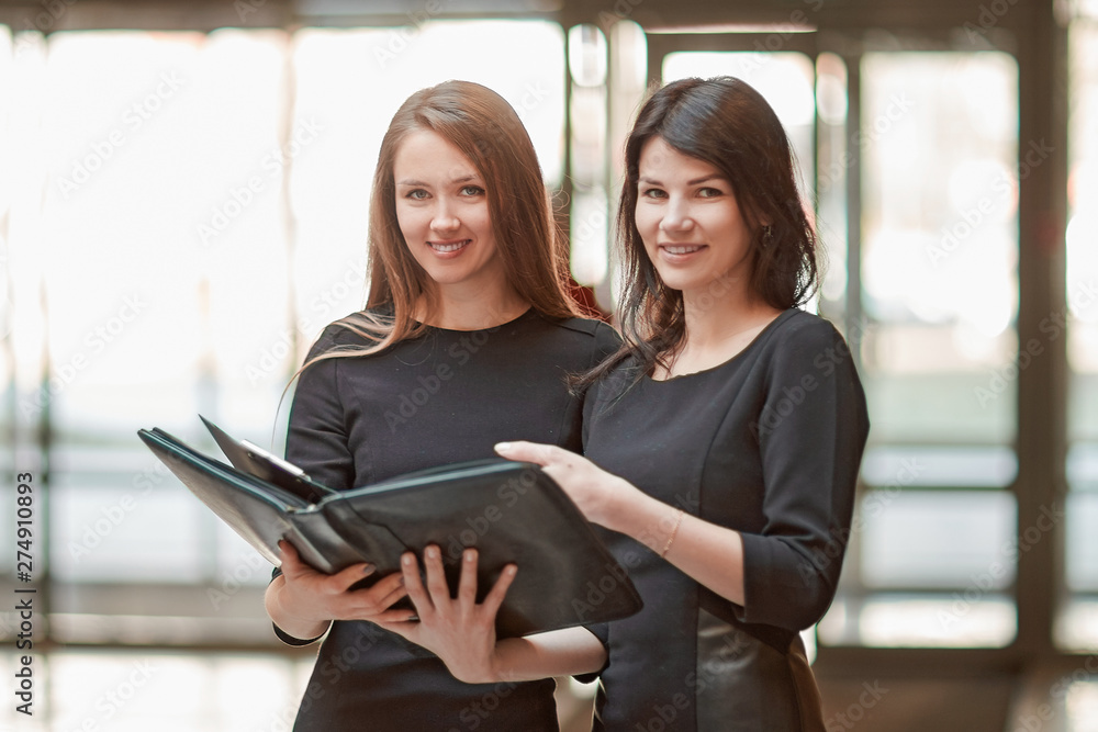 two business women read business documents standing in the office lobby. two business women read business documents standing in the office lobby.