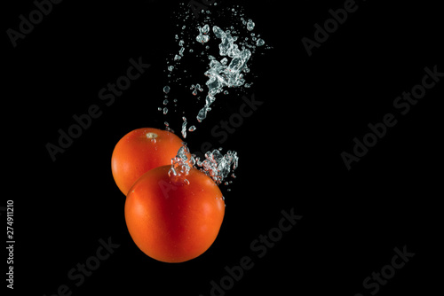 tomatoes under water with splashes on a black background