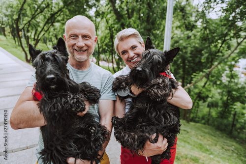 Smiling adult couple holding two black dogs in park photo