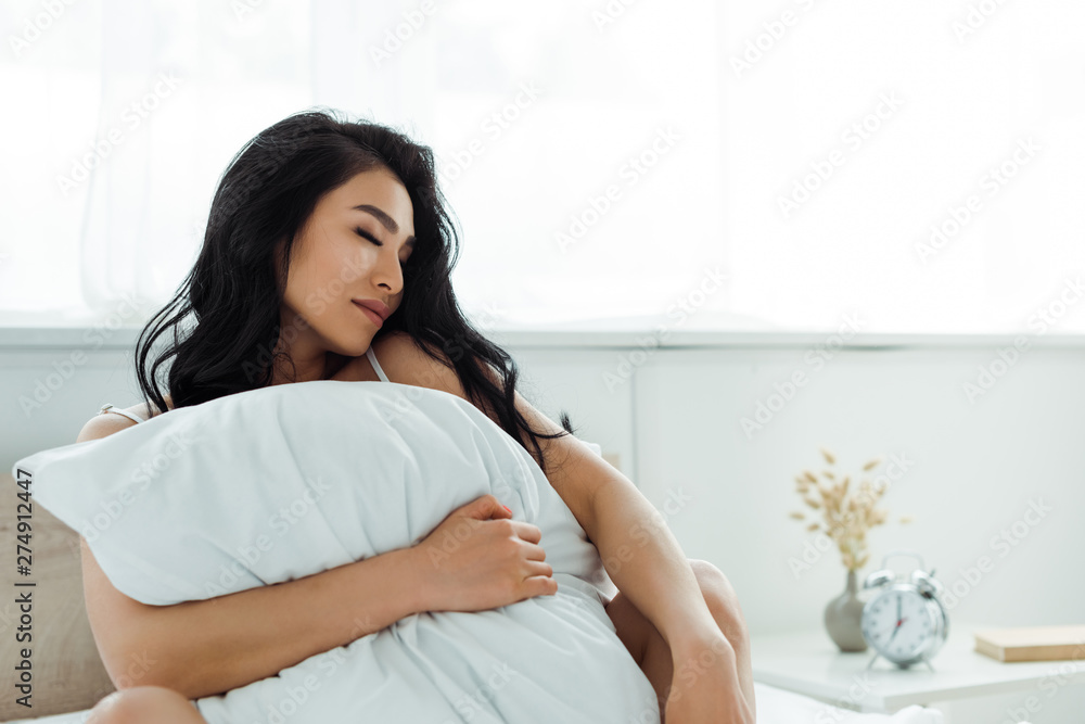 attractive asian woman with closed eyes holding pillow in bedroom attractive asian woman with closed eyes holding pillow in bedroom
