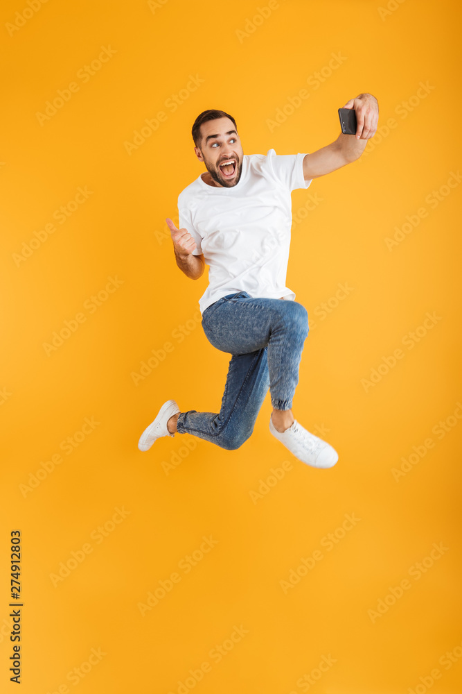 Full length photo of joyful caucasian man having beard taking selfie on cellphone and showing thumb up