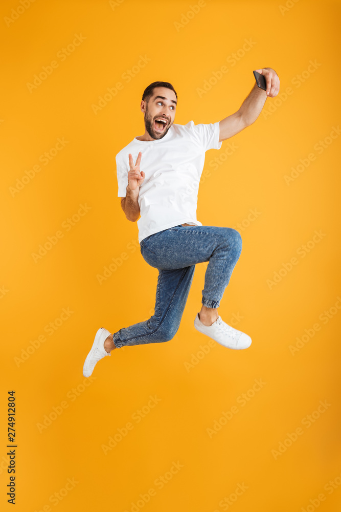 Full length photo of happy caucasian man having beard taking selfie on cellphone and showing peace sign