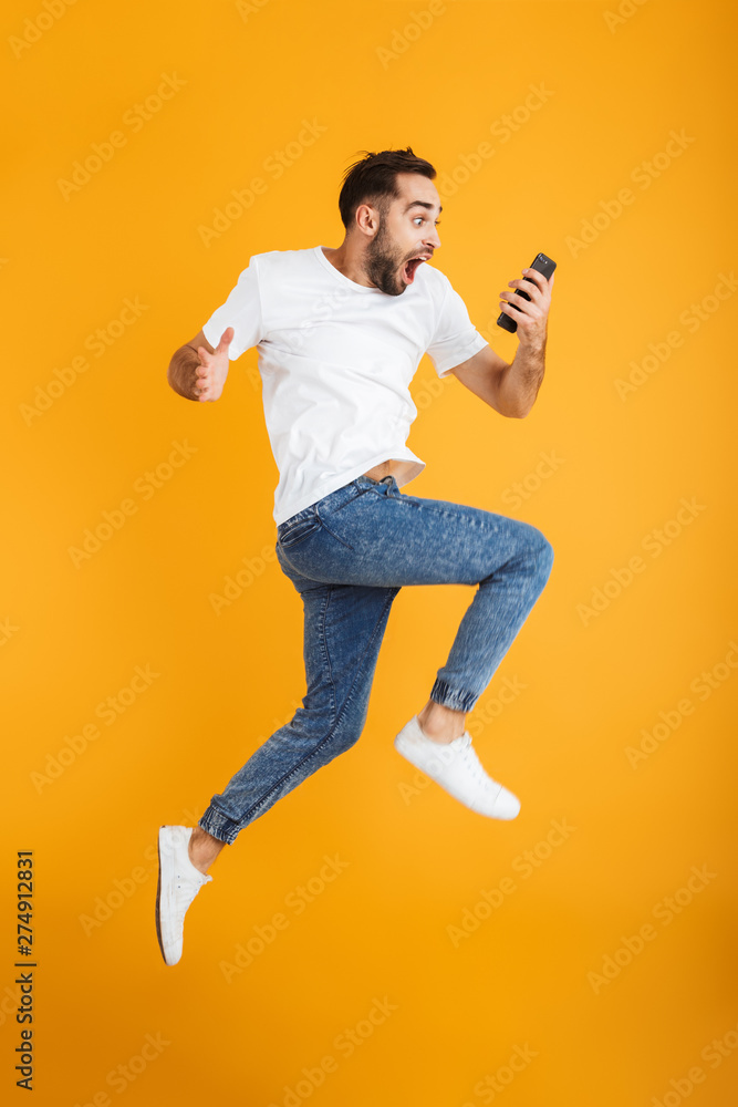 Full length photo of shocked caucasian man having beard wondering and holding cellphone while jumping Full length photo of shocked caucasian man having beard wondering and holding cellphone while jumping