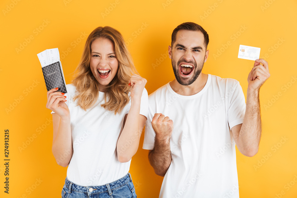 Image of delighted couple rejoicing while holding credit card and passport with travel tickets Image of delighted couple rejoicing while holding credit card and passport with travel tickets