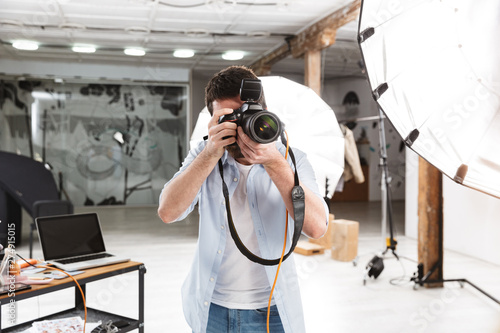 Portrait of young brunette photographer man shooting model with professional camera in studio photo