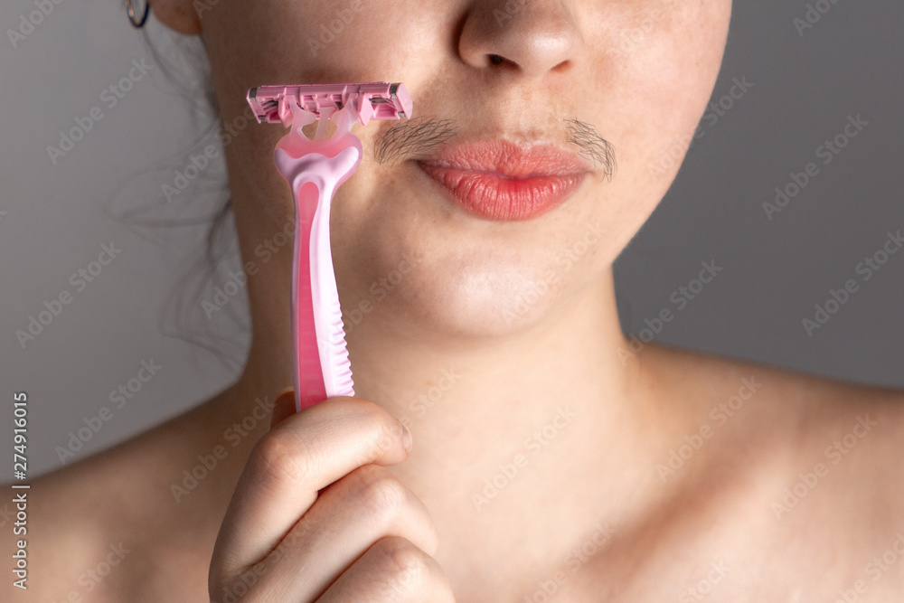 A young woman with a mustache winces, touching her face with a razor. The  concept of getting rid of unwanted facial hair. Close up Stock Photo |  Adobe Stock