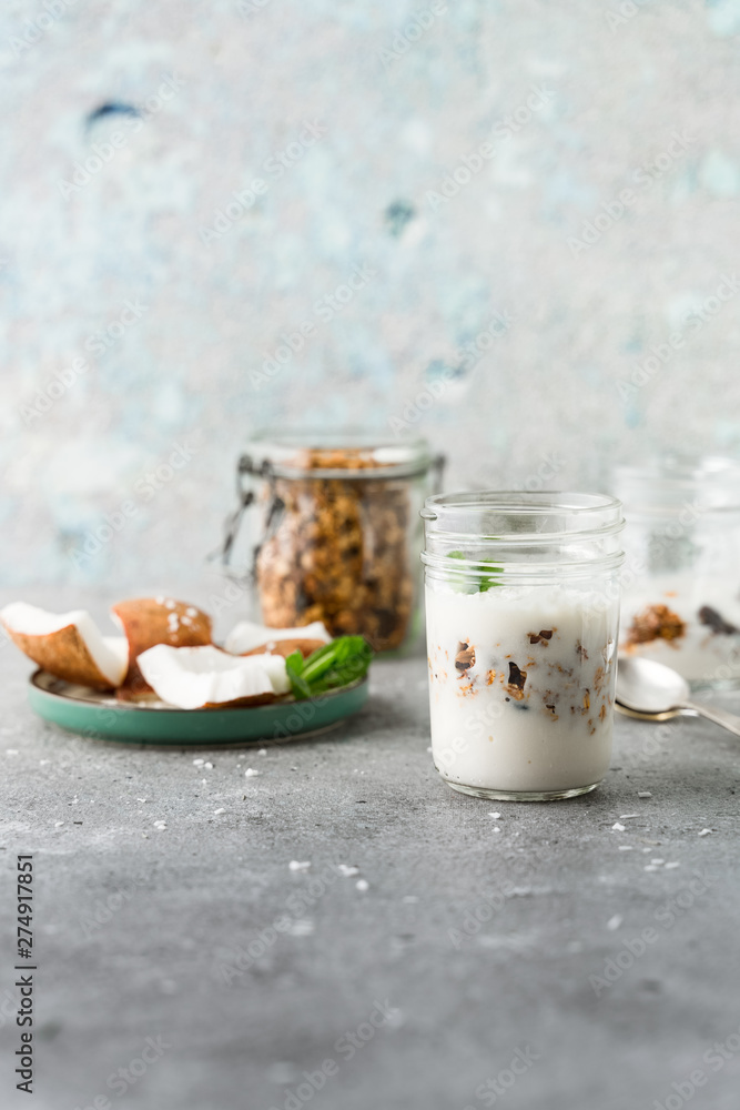 Homemade layered vegan dessert of baked granola and coconut yogurt in glass jar on gray background Homemade layered vegan dessert of baked granola and coconut yogurt in glass jar on gray background