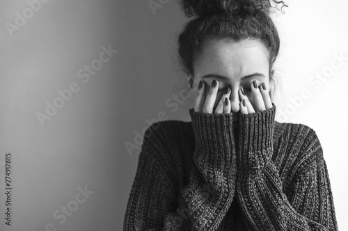 Fototapeta Close up of teenager with depression and bulimia sitting alone in dark room. She covers her face with hands. Mental problems with depression and bulimia. Black nad white photo.