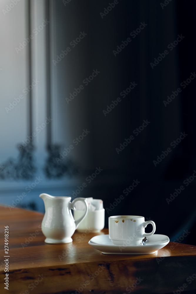 Coffee cup, milk jar, and sugar on wooden table in restaurant interior