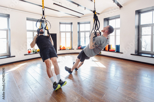 Two strong male athletes are engaged in the hall with to the trx system. Concept of team spirit and the trend of a healthy lifestyle