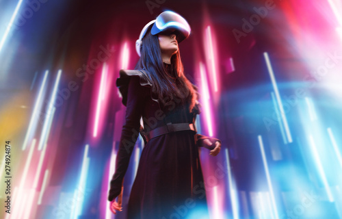 Beautiful woman in futuristic dress over dark background. Girl in glasses of virtual reality. Augmented reality, game, future technology, robots and people concept. VR. Neon light.