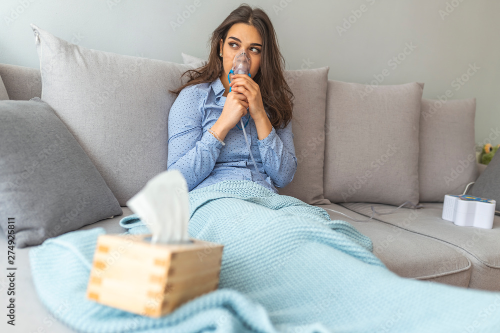 Woman using asthma machine at home. Sick beautiful female in blue cloth hold nasal mask with respiratory problem at home. Woman makes inhalation nebulizer at home Woman using asthma machine at home. Sick beautiful female in blue cloth hold nasal mask with respiratory problem at home. Woman makes inhalation nebulizer at home