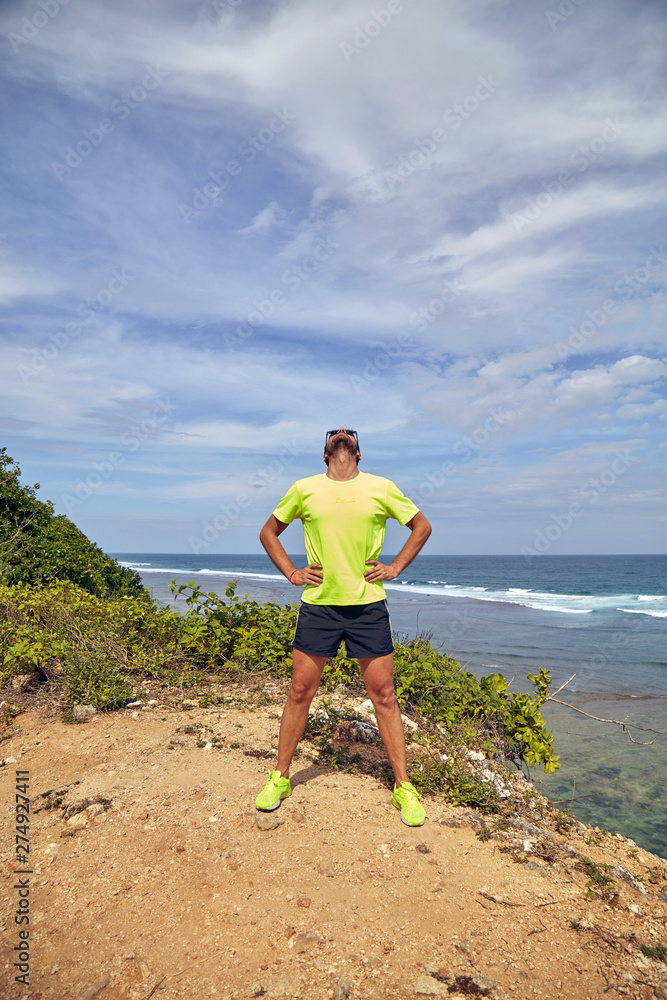 Sportsman stretching on a tropical exotic cliff near the ocean.