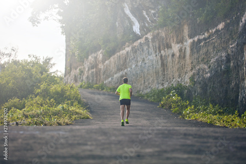 Fototapeta Man jogging on a downhill / uphill in suburb mountain road.