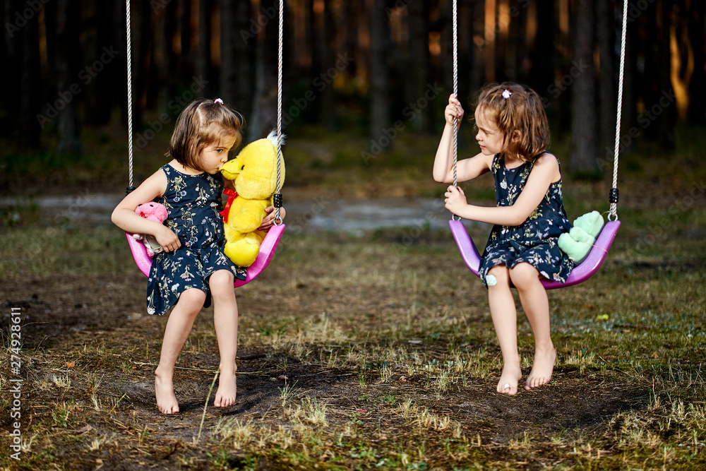 Two cute little girls on swing in forest on summer day