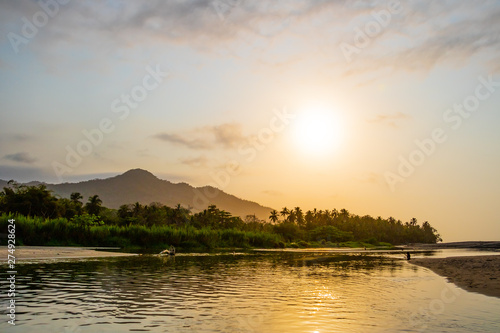 A wide river flows through the tropical rainforest of South America at a beautiful sunset where people bathe and enjoy life, Colombia Palomino