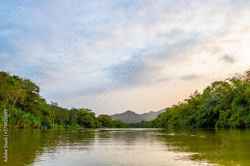 A wide river flows through the tropical rainforest of South America at a beautiful sunset where people bathe and enjoy life, Colombia Palomino