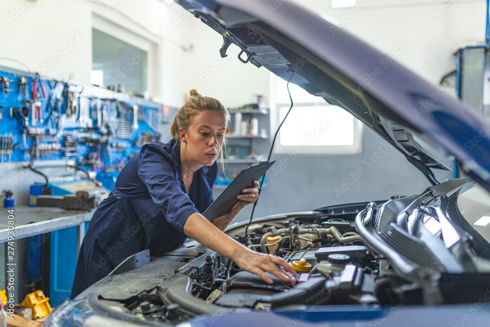 Lovely female auto mechanic smiling, examining engine of an automobile. Cheerful female car technician enjoying working at the garage, copy space. Repair, car service concept Lovely female auto mechanic smiling, examining engine of an automobile. Cheerful female car technician enjoying working at the garage, copy space. Repair, car service concept