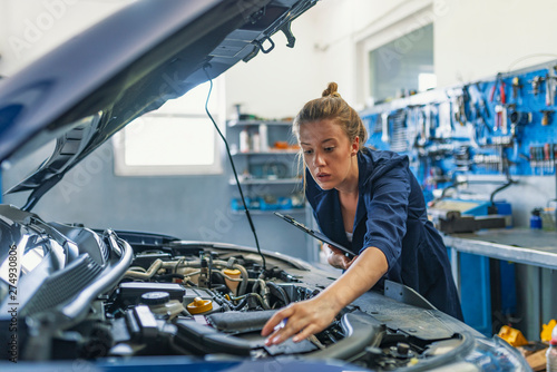 Mechanic working under the hood at the repair garage. Portrait of a happy mechanic woman working on a car in an auto repair shop. Female mechanic working on car